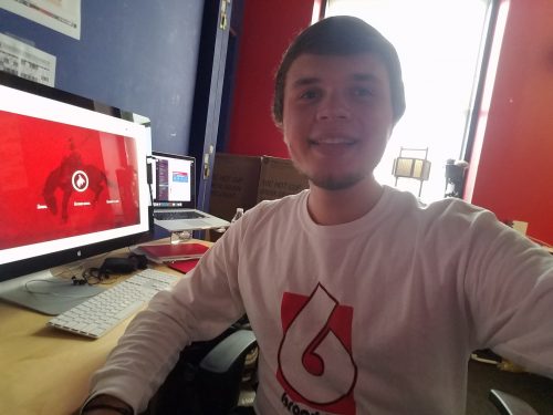 Young man in white sweater working at computer desk with red monitor display in colorful office workspace