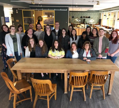 Group of young professionals posing together around wooden table in modern office or coworking space