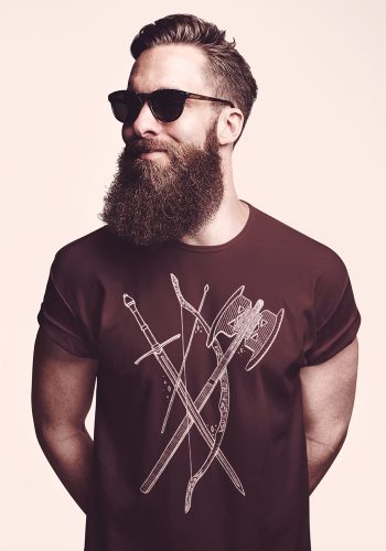 Bearded man in sunglasses wearing burgundy t-shirt with crossed medieval weapons design on light background
