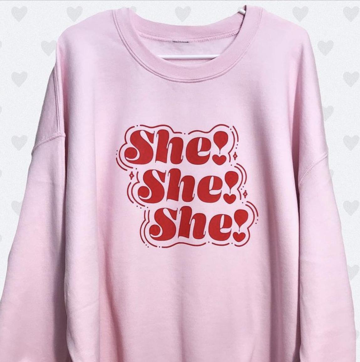Pink long-sleeve shirt with red She! She! She! text in retro bubble font style on light background