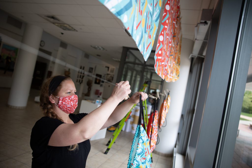 Woman in red floral mask hanging colorful patterned fabrics on display rack in bright retail store interior