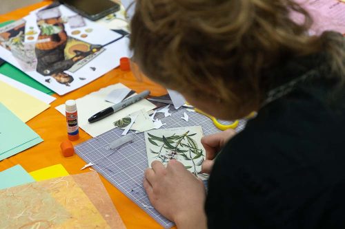 Person crafting with botanical leaf prints on cutting mat surrounded by colorful paper and art supplies