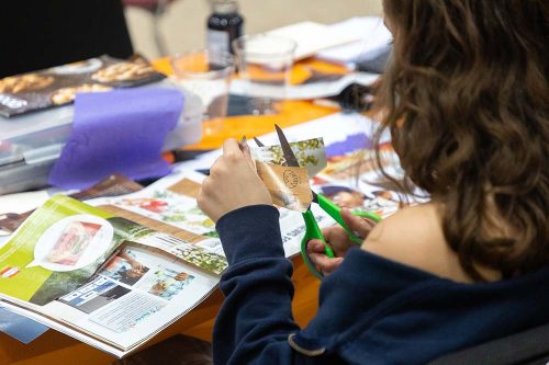 Student cutting photos from magazines with green scissors for art project collage at classroom desk