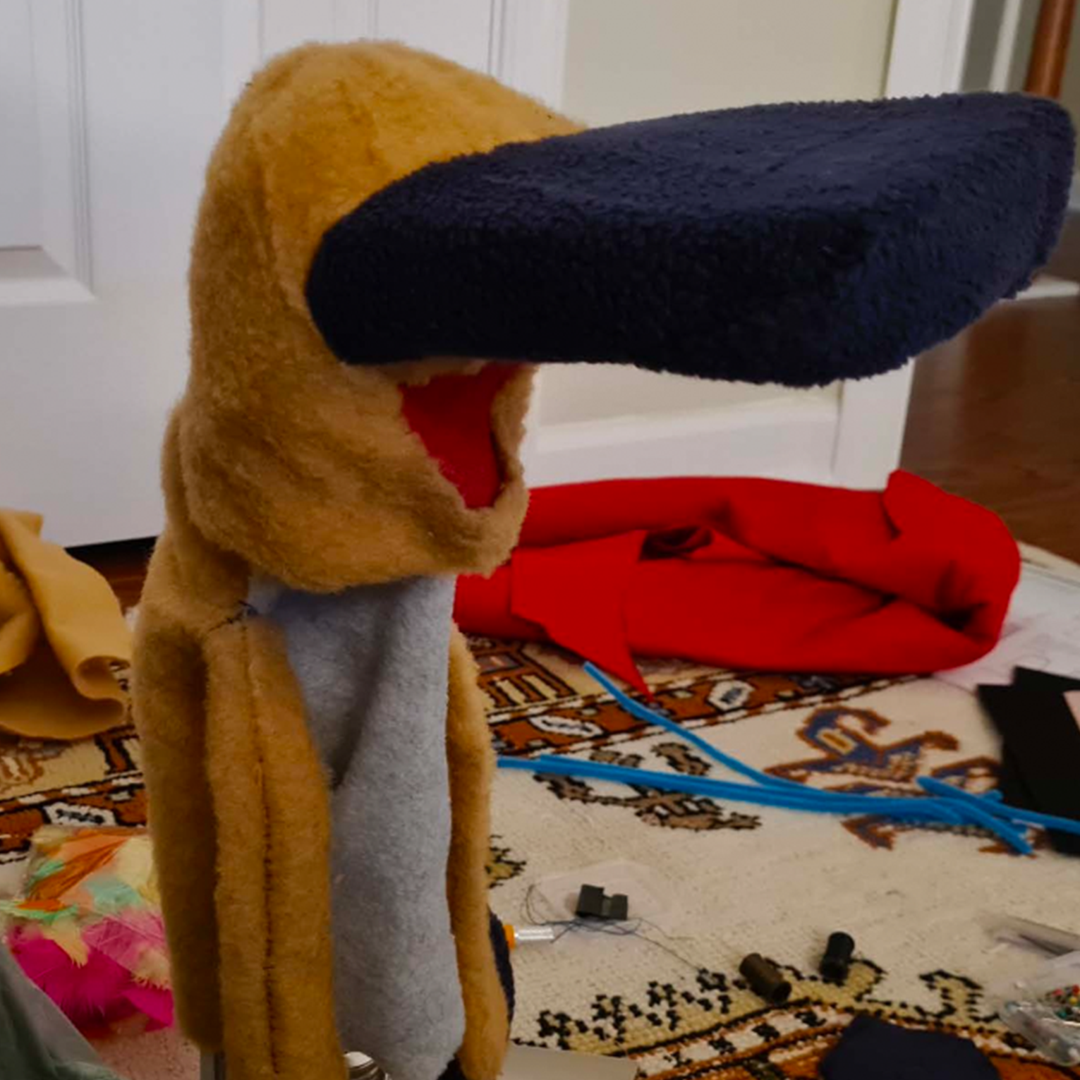 Colorful felt craft project with yellow duck head, navy blue beak, and red fabric on wooden chair with craft supplies