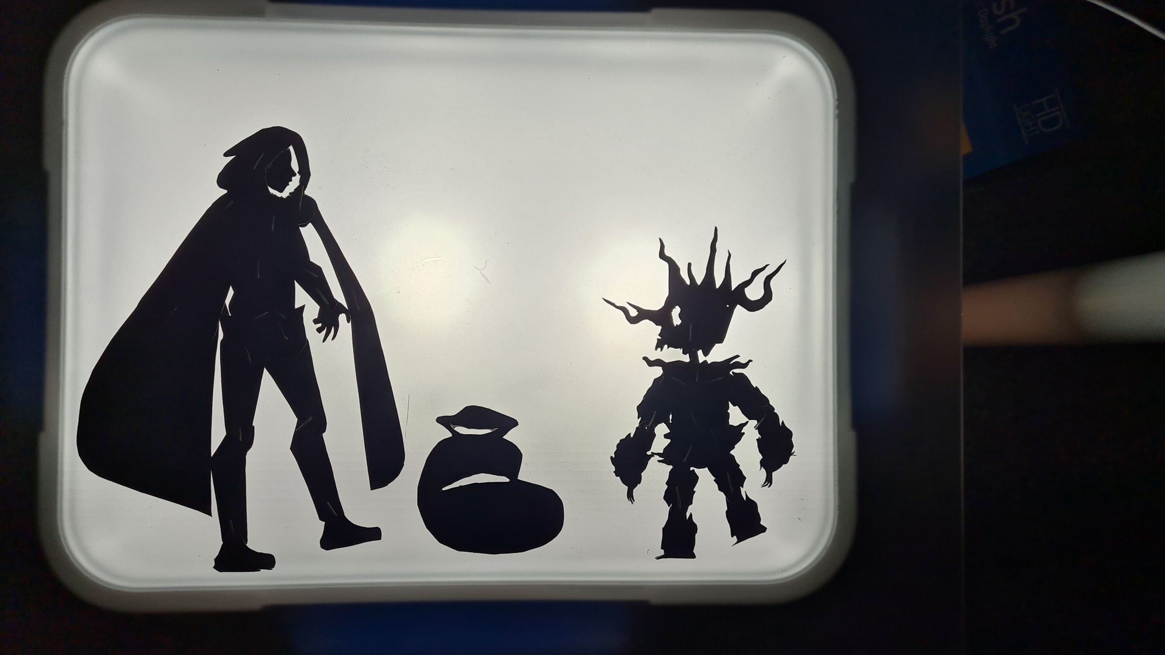 Black silhouette decals on white surface showing tall figure with cape next to spiky armored character and round objects