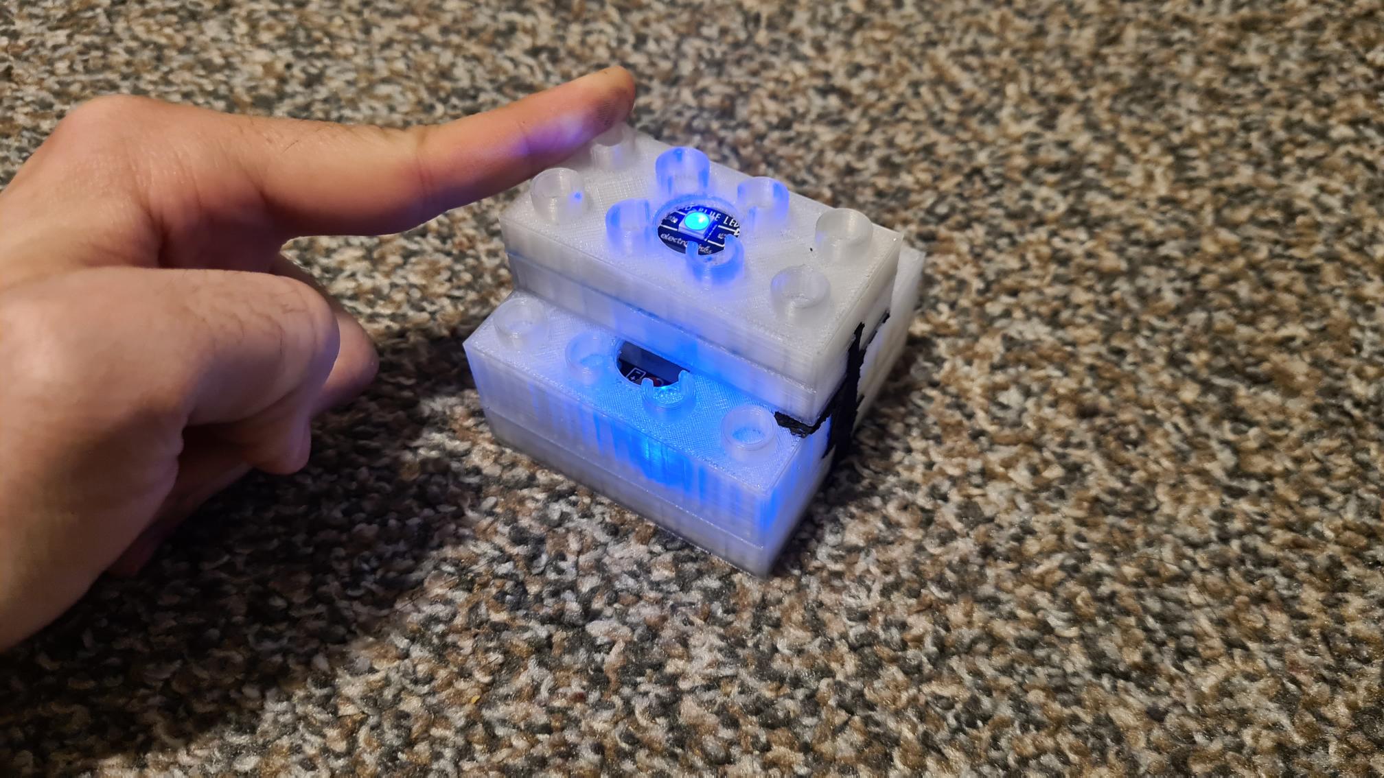 Hand hovering over white 3D printed electronic device with blue LED lights on granite countertop surface