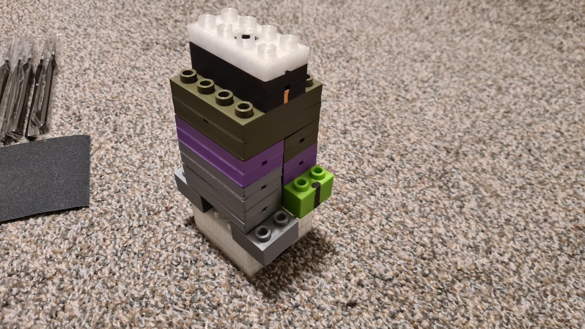 LEGO tower with white, black, green, purple and gray blocks stacked on carpeted floor