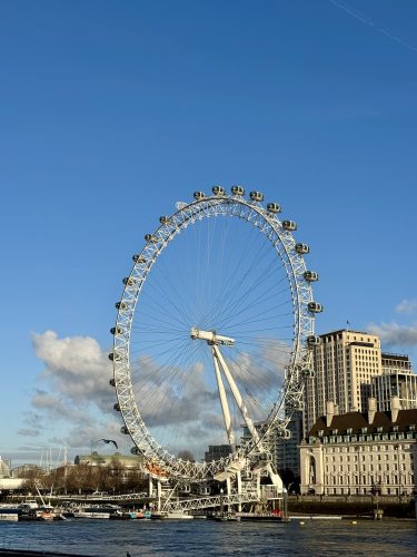 London Eye ferris wheel on Thames River with city buildings and blue sky in background